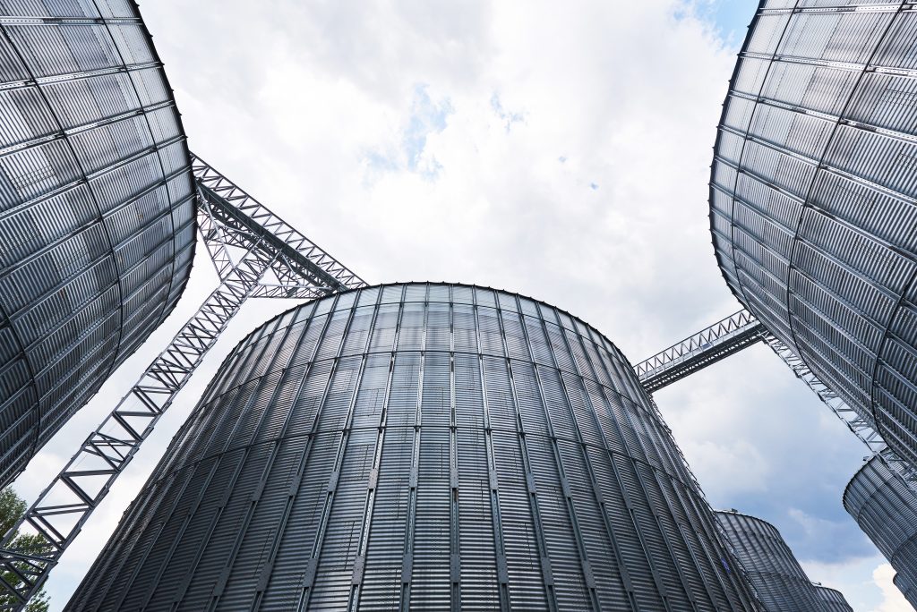 Agricultural Silos. Building Exterior. Storage and drying of grains, wheat, corn, soy, sunflower against the blue sky with white clouds