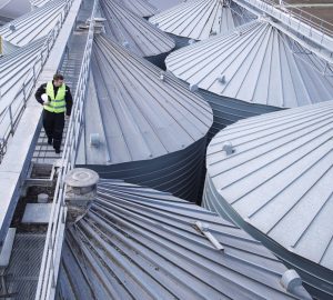 Factory worker walking on metal platform and doing visual inspection on industrial food storage tanks or silos.